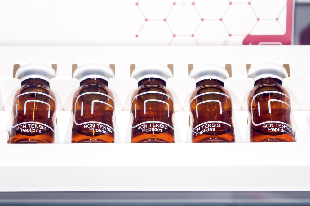 Five amber glass vials of BCN Tensis Peptides with silver caps displayed in a white tray